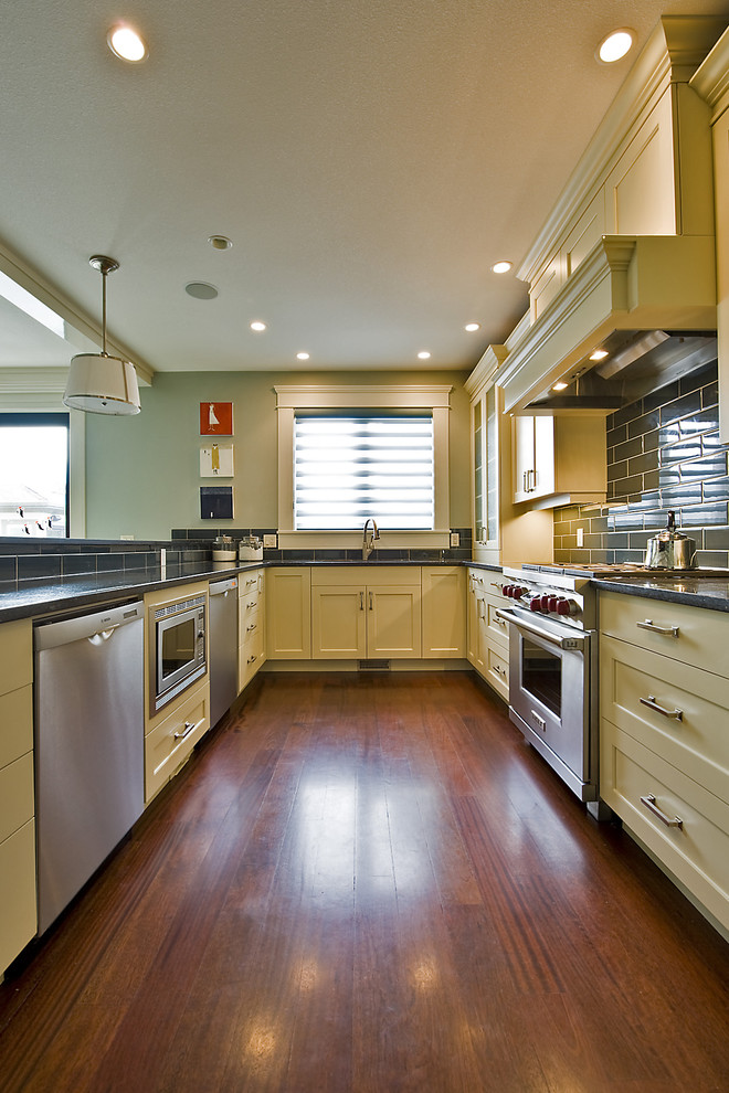 Modern inredning av ett kök, med rostfria vitvaror, luckor med infälld panel, gula skåp och stänkskydd i tunnelbanekakel