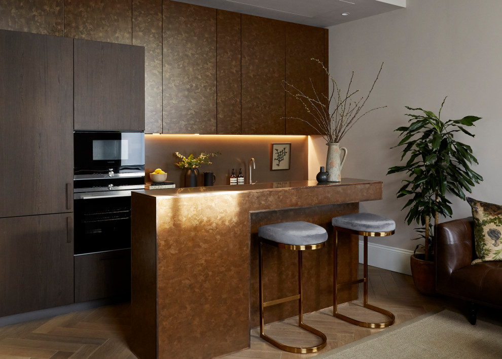 This is an example of a small contemporary open plan kitchen in London with an integrated sink, brown splashback, black appliances, medium hardwood flooring, an island, brown floors, brown worktops and composite countertops.