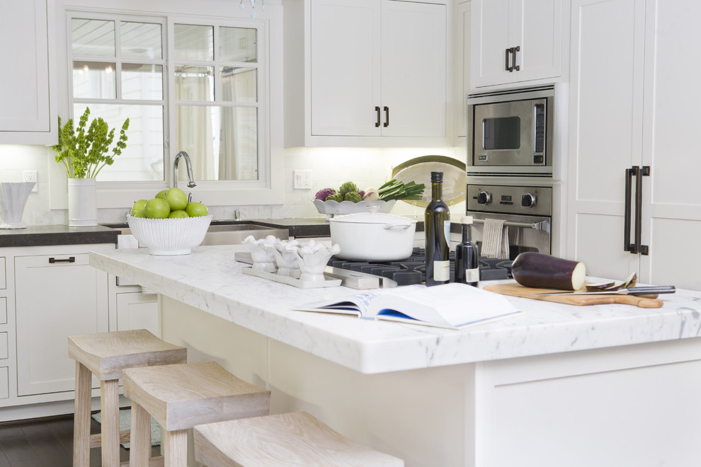 Large trendy u-shaped dark wood floor enclosed kitchen photo in Orange County with stainless steel appliances, a farmhouse sink, shaker cabinets, white cabinets, soapstone countertops, white backsplash, stone tile backsplash and an island