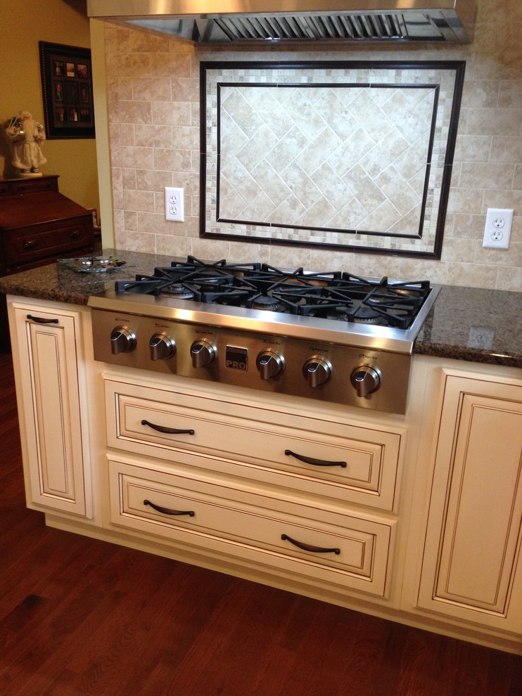 Immagine di una cucina chic con ante con bugna sagomata, ante beige, top in granito, paraspruzzi con piastrelle in ceramica, elettrodomestici neri e pavimento in legno massello medio