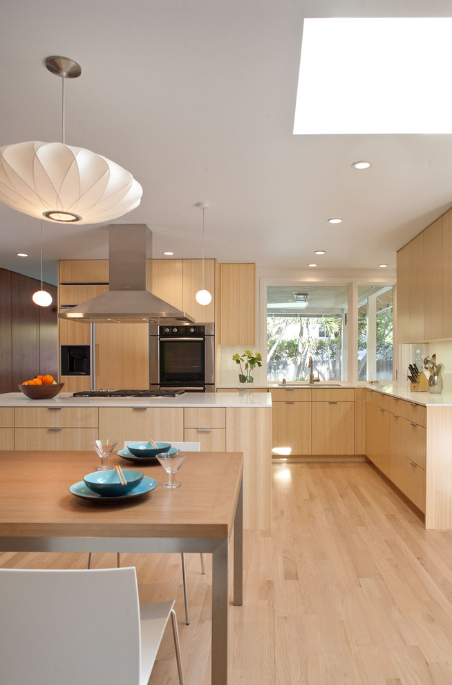 Идея дизайна: угловая кухня-гостиная в стиле модернизм с техникой из нержавеющей стали, врезной мойкой, плоскими фасадами, фасадами цвета дерева среднего тона, столешницей из кварцевого агломерата и белым фартуком