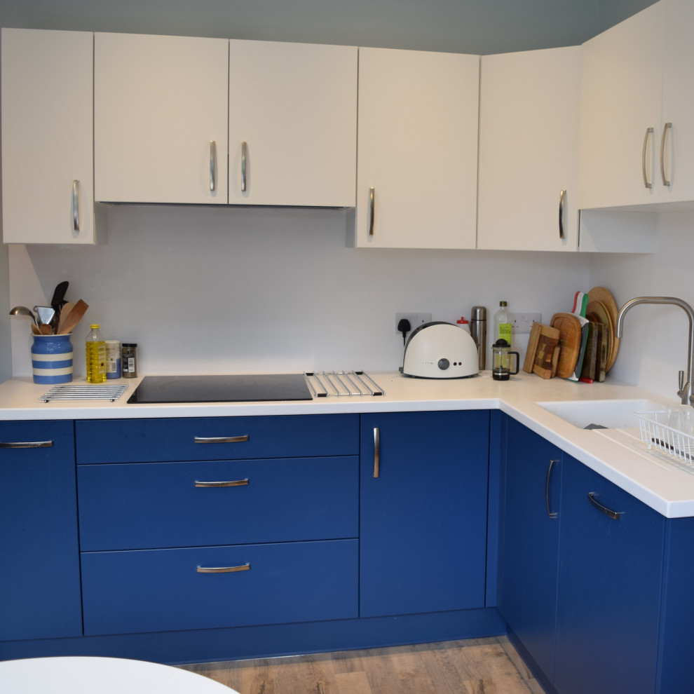 Exempel på ett litet, avskilt modernt vit vitt l-kök, med en enkel diskho, släta luckor, blå skåp, bänkskiva i koppar, svarta vitvaror, laminatgolv, en halv köksö och beiget golv