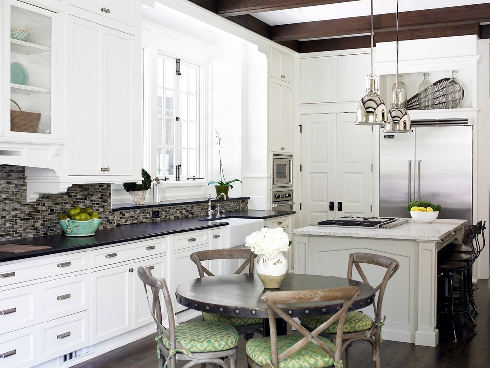 Mid-sized transitional l-shaped dark wood floor eat-in kitchen photo in Atlanta with stainless steel appliances, a farmhouse sink, white cabinets, black backsplash, glass tile backsplash, granite countertops, shaker cabinets and an island
