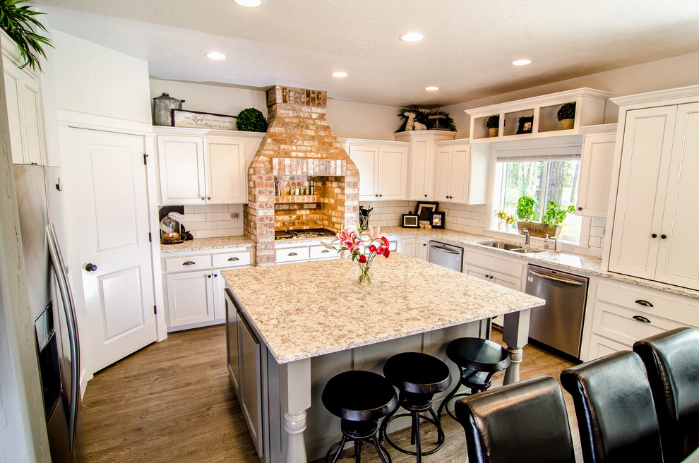Amerikansk inredning av ett stort kök, med en undermonterad diskho, luckor med infälld panel, vita skåp, marmorbänkskiva, vitt stänkskydd, stänkskydd i keramik, rostfria vitvaror och en köksö