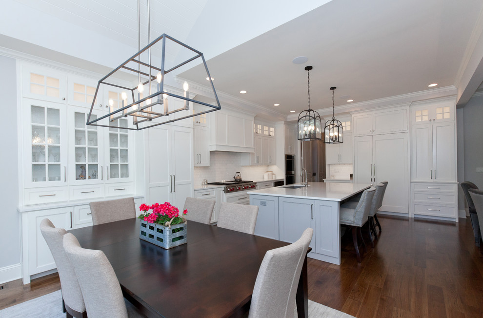 Example of a mid-sized transitional l-shaped medium tone wood floor and brown floor eat-in kitchen design in Chicago with an undermount sink, shaker cabinets, white cabinets, quartzite countertops, white backsplash, subway tile backsplash, paneled appliances, an island and white countertops