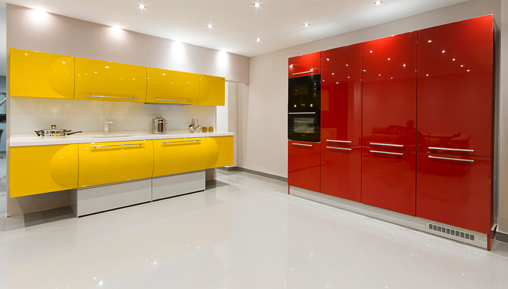 Стильный дизайн: угловая кухня-гостиная среднего размера в стиле модернизм с врезной мойкой, желтыми фасадами, столешницей из акрилового камня, желтым фартуком, фартуком из стекла, черной техникой и полом из керамогранита - последний тренд