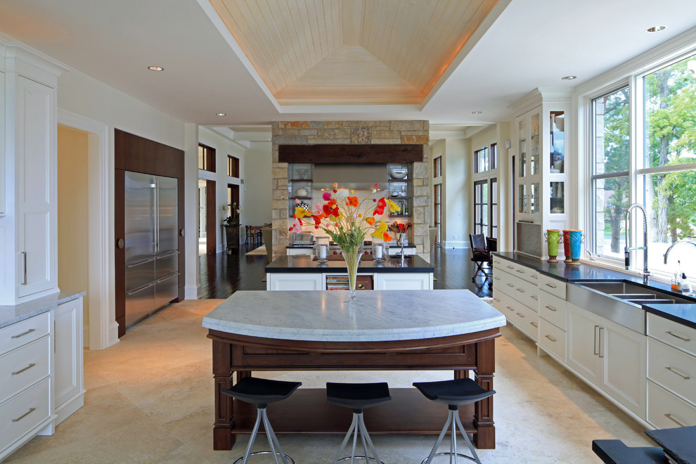 Modern inredning av ett kök, med rostfria vitvaror, en trippel diskho, vita skåp, travertin golv och flera köksöar