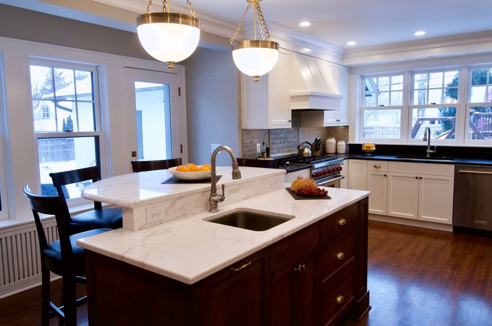 Klassisk inredning av ett stort vit vitt u-kök, med en undermonterad diskho, luckor med infälld panel, vita skåp, bänkskiva i kvarts, brunt stänkskydd, stänkskydd i glaskakel, rostfria vitvaror, mellanmörkt trägolv, en köksö och brunt golv