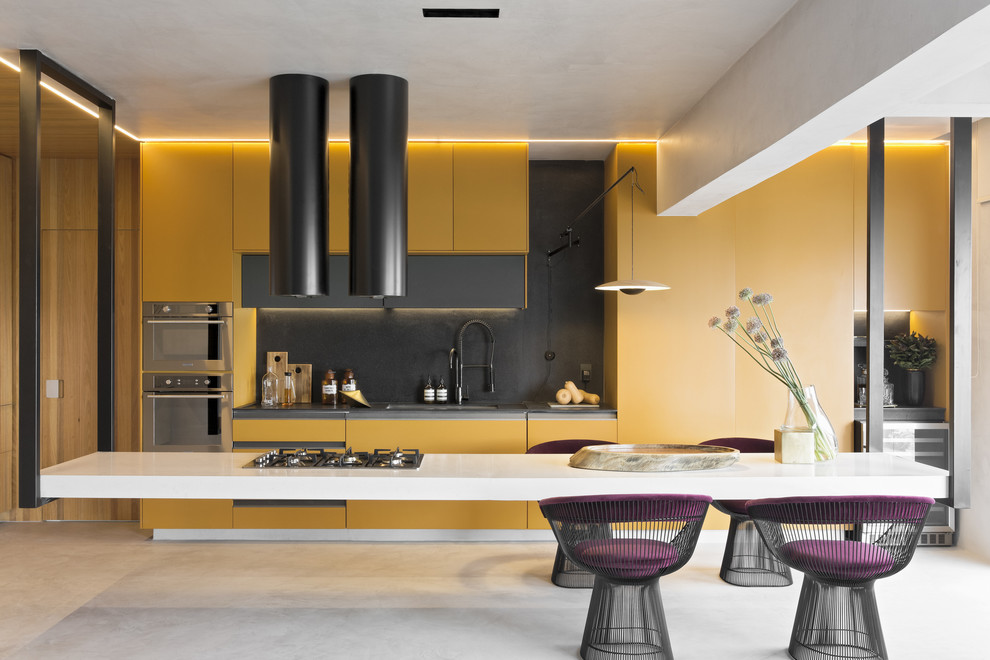 Пример оригинального дизайна: большая параллельная кухня в современном стиле с обеденным столом, желтыми фасадами, желтым фартуком, серым полом, плоскими фасадами, бетонным полом и островом