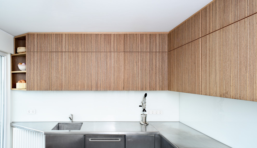 Réalisation d'une cuisine américaine minimaliste en bois foncé avec un plan de travail en inox et une crédence blanche.