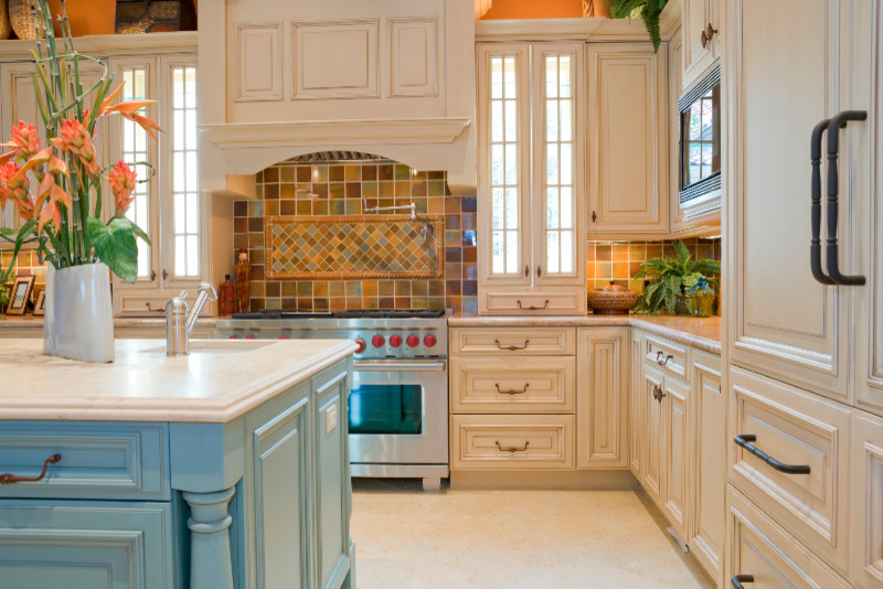 Lantlig inredning av ett stort kök, med en nedsänkt diskho, beige skåp, granitbänkskiva, stänkskydd i mosaik, rostfria vitvaror, en köksö, luckor med upphöjd panel och flerfärgad stänkskydd
