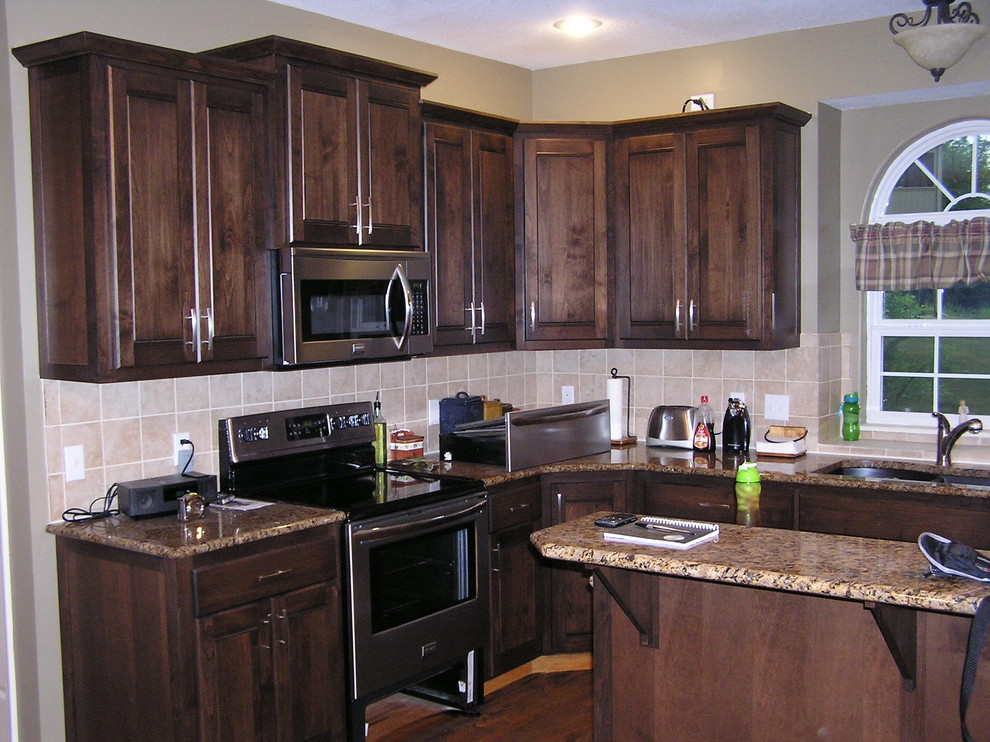 Example of a mid-sized classic l-shaped medium tone wood floor and brown floor kitchen design in Kansas City with a double-bowl sink, raised-panel cabinets, dark wood cabinets, granite countertops, beige backsplash, ceramic backsplash, stainless steel appliances and an island