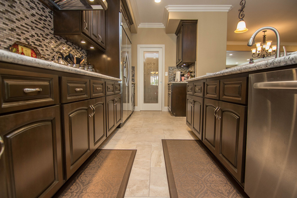 Example of a large transitional travertine floor open concept kitchen design in Los Angeles with raised-panel cabinets, dark wood cabinets, solid surface countertops, stainless steel appliances and an island