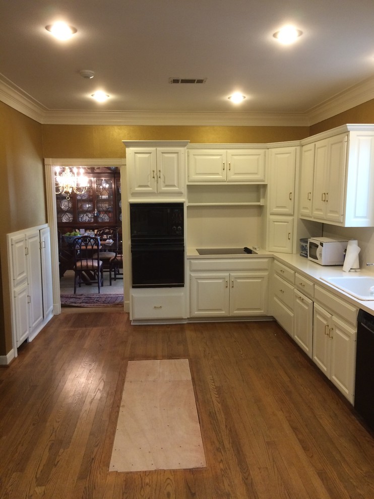 Eat-in kitchen - mid-sized traditional l-shaped medium tone wood floor eat-in kitchen idea in Austin with raised-panel cabinets, white cabinets, solid surface countertops, yellow backsplash, black appliances and no island