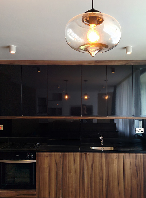 Exempel på ett mellanstort modernt kök, med en undermonterad diskho, släta luckor, skåp i mörkt trä, granitbänkskiva, svart stänkskydd, glaspanel som stänkskydd, rostfria vitvaror, mellanmörkt trägolv och en köksö