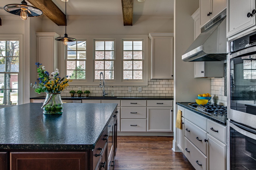 Rustik inredning av ett stort kök, med en undermonterad diskho, vita skåp, granitbänkskiva, vitt stänkskydd, rostfria vitvaror, mellanmörkt trägolv och en köksö