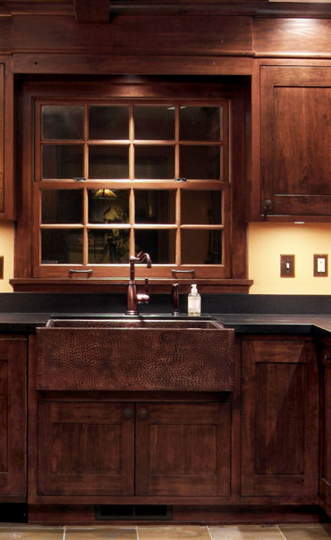 Elegant l-shaped eat-in kitchen photo in Portland with a farmhouse sink, raised-panel cabinets, dark wood cabinets, granite countertops, black backsplash, paneled appliances and stone slab backsplash