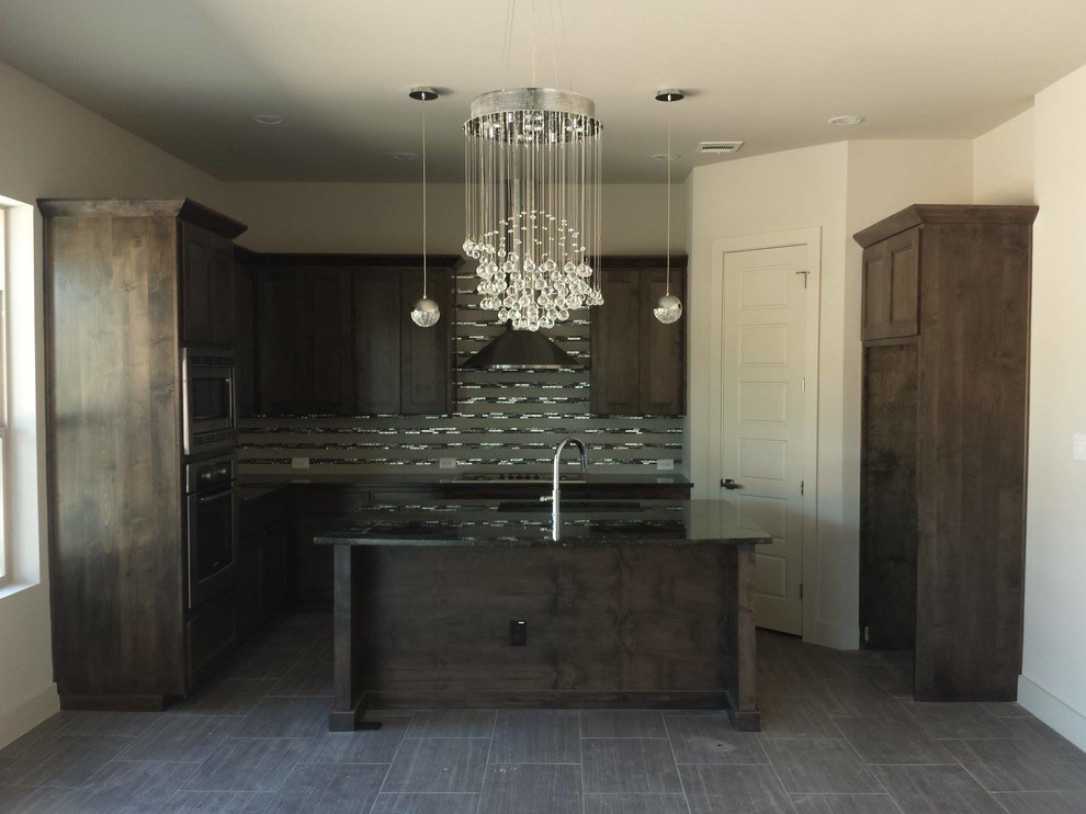 L-shaped linoleum floor eat-in kitchen photo in Austin with recessed-panel cabinets, dark wood cabinets, solid surface countertops, gray backsplash, glass tile backsplash, stainless steel appliances and an island