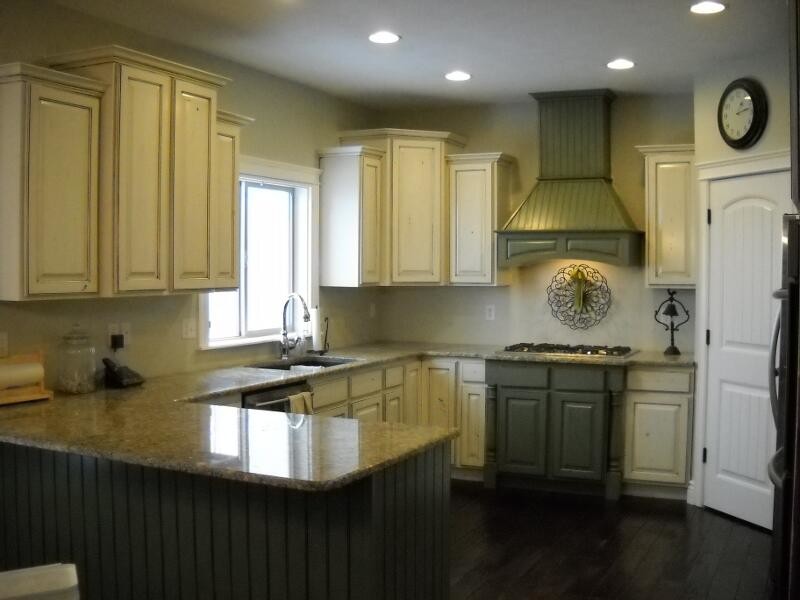 Inredning av ett mellanstort kök, med en dubbel diskho, luckor med upphöjd panel, beige skåp, marmorbänkskiva, grönt stänkskydd, stänkskydd i keramik, svarta vitvaror och mörkt trägolv