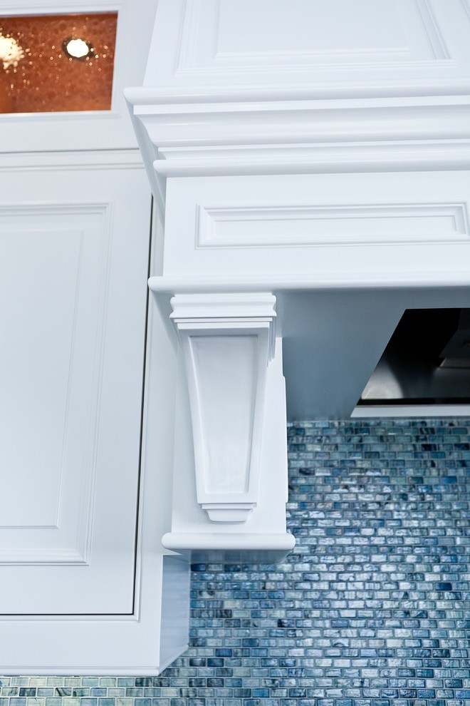 Cette photo montre une grande cuisine américaine chic en U avec des portes de placard blanches, plan de travail en marbre, une crédence bleue, une crédence en carreau de verre et un électroménager en acier inoxydable.