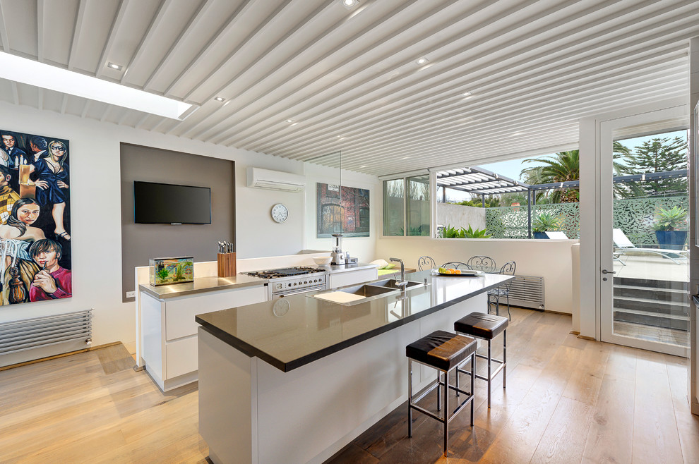 Große Moderne Wohnküche mit Doppelwaschbecken, weißen Schränken, Küchengeräten aus Edelstahl, hellem Holzboden und zwei Kücheninseln in Melbourne