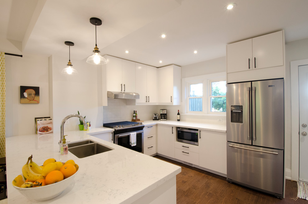 Exempel på ett mellanstort modernt kök, med en dubbel diskho, släta luckor, vita skåp, bänkskiva i kvarts, vitt stänkskydd, stänkskydd i tunnelbanekakel, rostfria vitvaror, mellanmörkt trägolv, en halv köksö och brunt golv