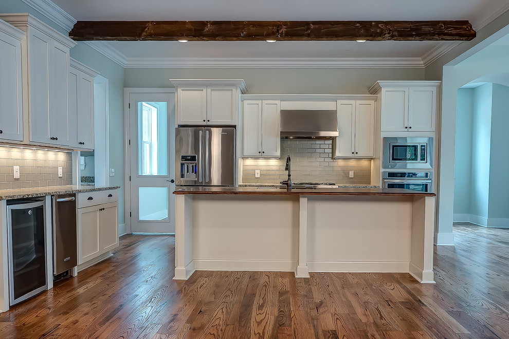Open concept kitchen - mid-sized traditional l-shaped medium tone wood floor open concept kitchen idea in Atlanta with a farmhouse sink, shaker cabinets, beige cabinets, granite countertops, gray backsplash, subway tile backsplash, stainless steel appliances and an island
