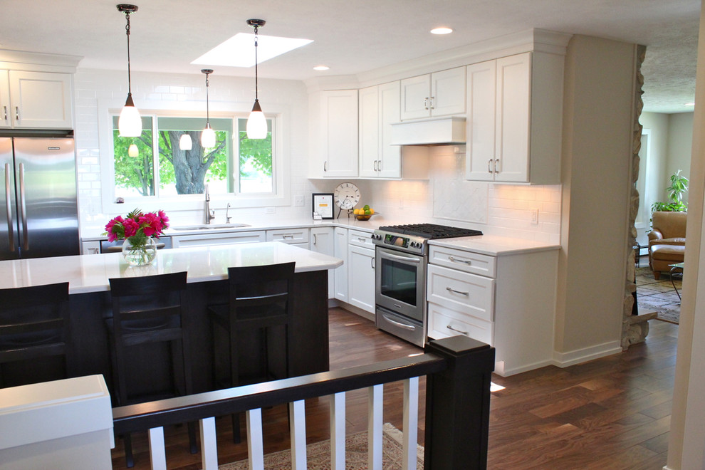 Example of a medium tone wood floor kitchen design in Grand Rapids with a drop-in sink, recessed-panel cabinets, white cabinets, white backsplash, stainless steel appliances and an island
