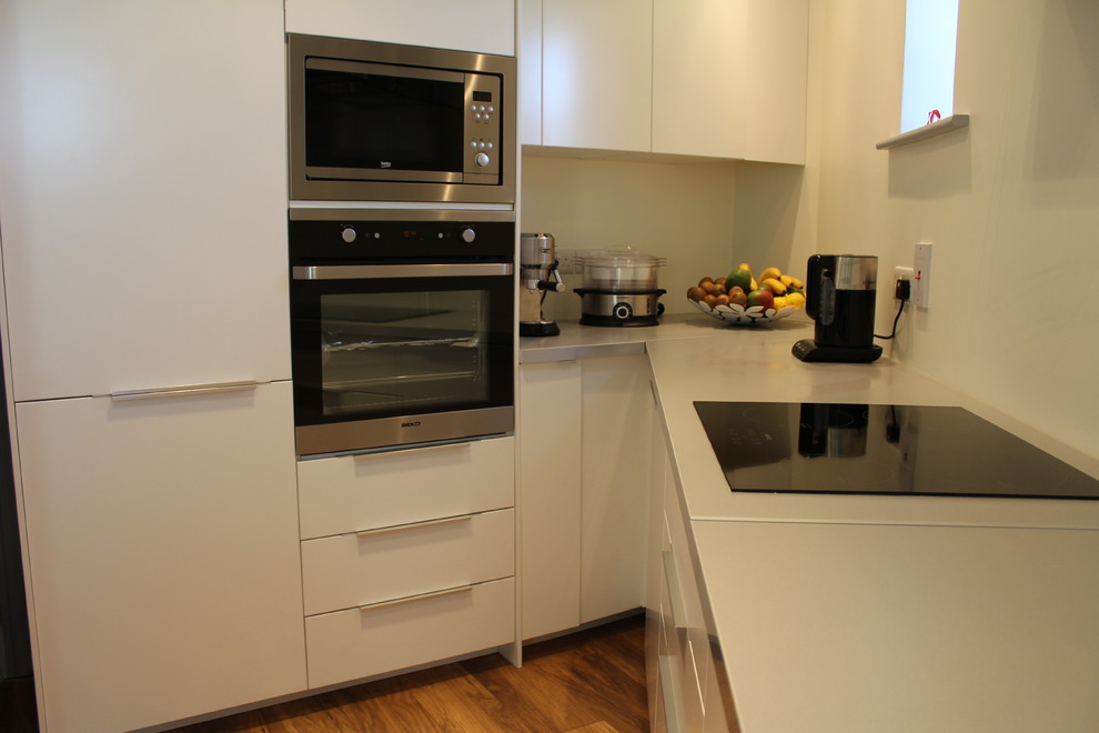 Photo of a medium sized modern l-shaped kitchen/diner in Dublin with white cabinets, medium hardwood flooring, no island, a single-bowl sink, laminate countertops, white splashback and stainless steel appliances.