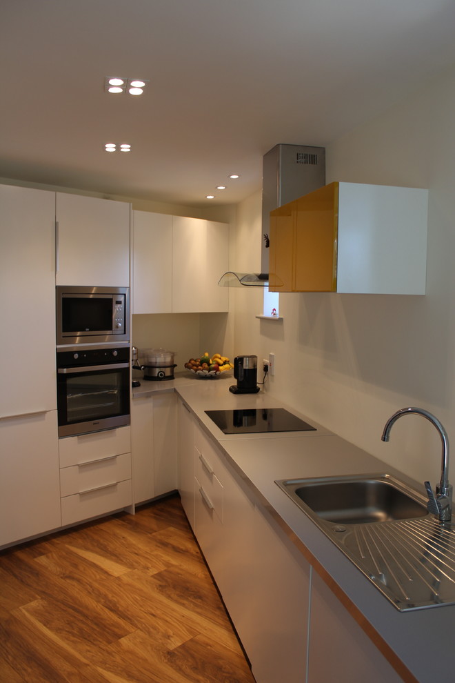 Mittelgroße Moderne Wohnküche ohne Insel in L-Form mit weißen Schränken, braunem Holzboden, Waschbecken, Laminat-Arbeitsplatte, Küchenrückwand in Weiß und Elektrogeräten mit Frontblende in Dublin