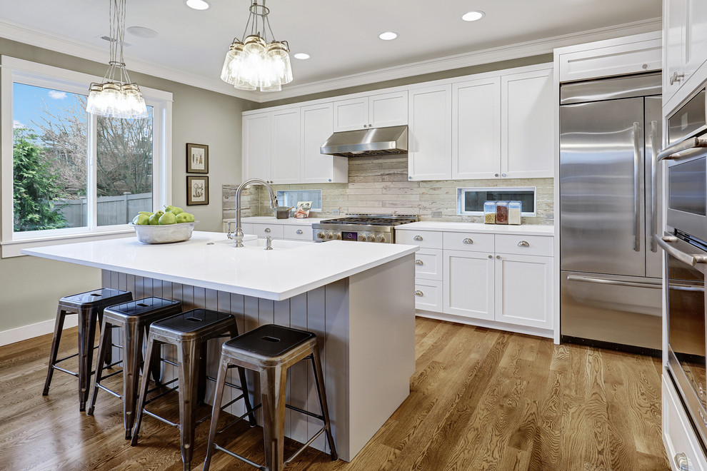 Traditional galley kitchen/diner in Seattle with recessed-panel cabinets, white cabinets, stainless steel appliances, light hardwood flooring, an island, a submerged sink, engineered stone countertops, grey splashback and porcelain splashback.