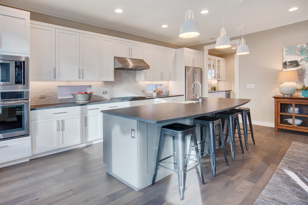 Inspiration for a classic galley kitchen/diner in Seattle with a belfast sink, recessed-panel cabinets, white cabinets, granite worktops, grey splashback, ceramic splashback, stainless steel appliances, medium hardwood flooring and an island.