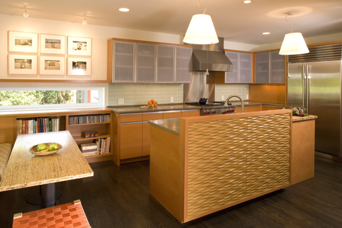 Bild på ett litet funkis kök, med släta luckor, skåp i rostfritt stål, bänkskiva i täljsten, grönt stänkskydd, stänkskydd i glaskakel, rostfria vitvaror, mörkt trägolv och en köksö