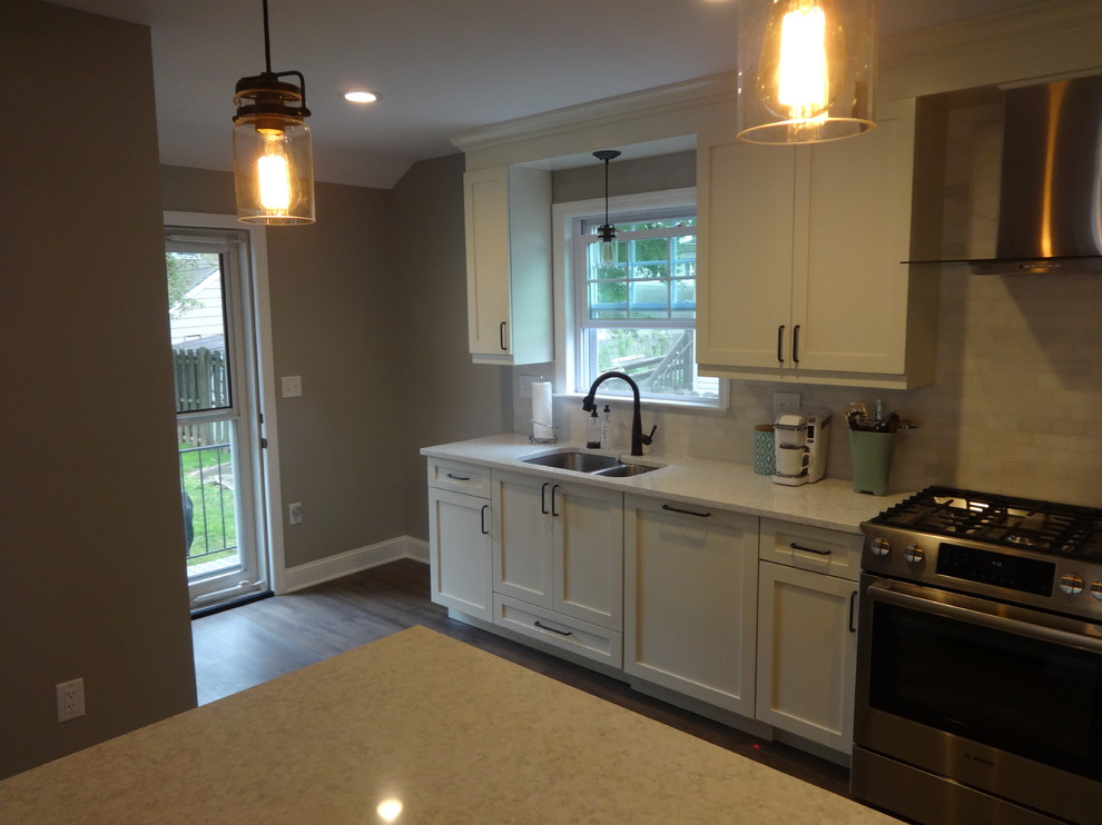 Modern inredning av ett stort linjärt kök och matrum, med en dubbel diskho, skåp i shakerstil, vita skåp, bänkskiva i kvarts, rostfria vitvaror, laminatgolv, en köksö och brunt golv