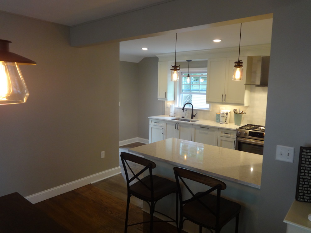 Foto på ett stort funkis linjärt kök och matrum, med en dubbel diskho, skåp i shakerstil, vita skåp, bänkskiva i kvarts, rostfria vitvaror, laminatgolv, en köksö och brunt golv