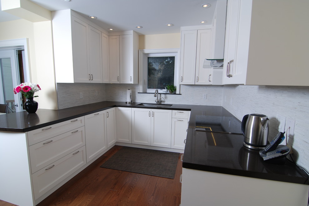 Photo of a medium sized contemporary u-shaped kitchen/diner in Toronto with a built-in sink, recessed-panel cabinets, white cabinets, engineered stone countertops, white splashback, ceramic splashback, stainless steel appliances, medium hardwood flooring and a breakfast bar.