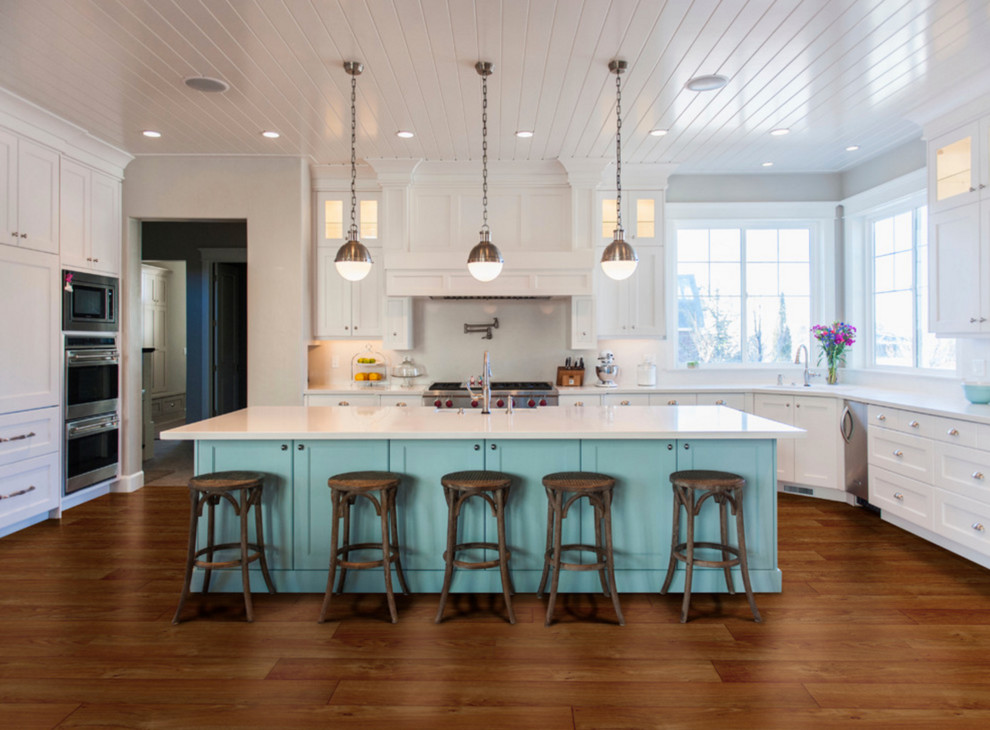 Design ideas for a large coastal l-shaped open plan kitchen in Orange County with a submerged sink, shaker cabinets, white cabinets, engineered stone countertops, stainless steel appliances, laminate floors, an island, brown floors, white splashback and white worktops.