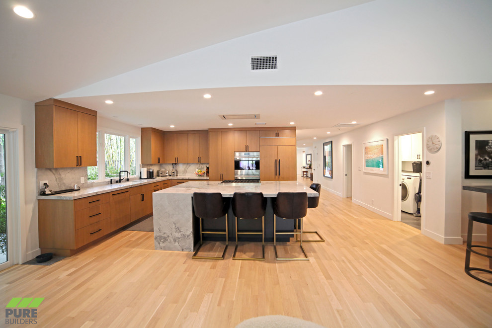Large trendy l-shaped light wood floor and beige floor eat-in kitchen photo in Los Angeles with an undermount sink, flat-panel cabinets, medium tone wood cabinets, marble countertops, marble backsplash, paneled appliances, an island, white backsplash and white countertops