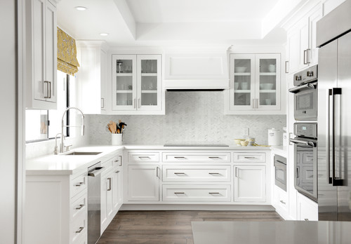 Premium RTA cabinets Canada: bright white L-shaped kitchen with shaker cabinets, glass-front uppers, paneled range hood, wide drawers, quartz counters, herringbone backsplash, and stainless wall ovens.