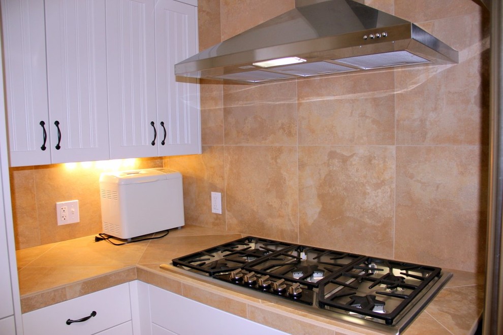 Aménagement d'une cuisine contemporaine avec un placard à porte shaker, plan de travail en marbre, une crédence beige, un électroménager en acier inoxydable et un sol en bois brun.