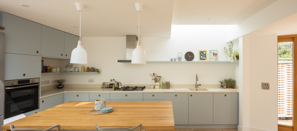 Photo of a medium sized contemporary l-shaped kitchen in Cambridgeshire with an integrated sink, flat-panel cabinets, blue cabinets, composite countertops, stainless steel appliances, an island and beige worktops.