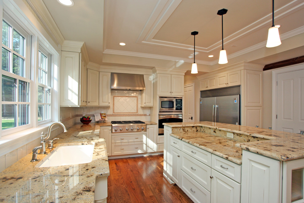 Lantlig inredning av ett kök, med en undermonterad diskho, luckor med upphöjd panel, beige skåp, vitt stänkskydd, stänkskydd i keramik, rostfria vitvaror och mellanmörkt trägolv