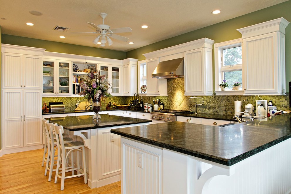 Bild på ett mellanstort vintage l-kök, med luckor med lamellpanel, vita skåp, laminatbänkskiva, grönt stänkskydd, stänkskydd i mosaik, ljust trägolv, en köksö, en nedsänkt diskho, rostfria vitvaror och brunt golv