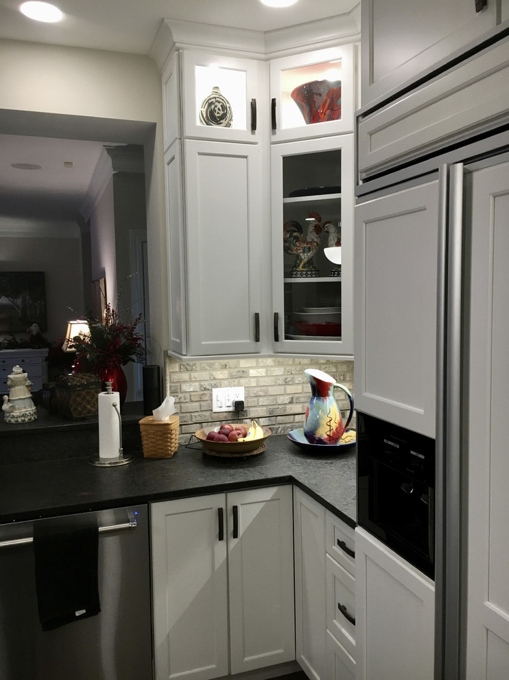 Modern inredning av ett stort kök, med en undermonterad diskho, luckor med infälld panel, vita skåp, granitbänkskiva, flerfärgad stänkskydd, stänkskydd i travertin, rostfria vitvaror, ljust trägolv, en köksö och beiget golv