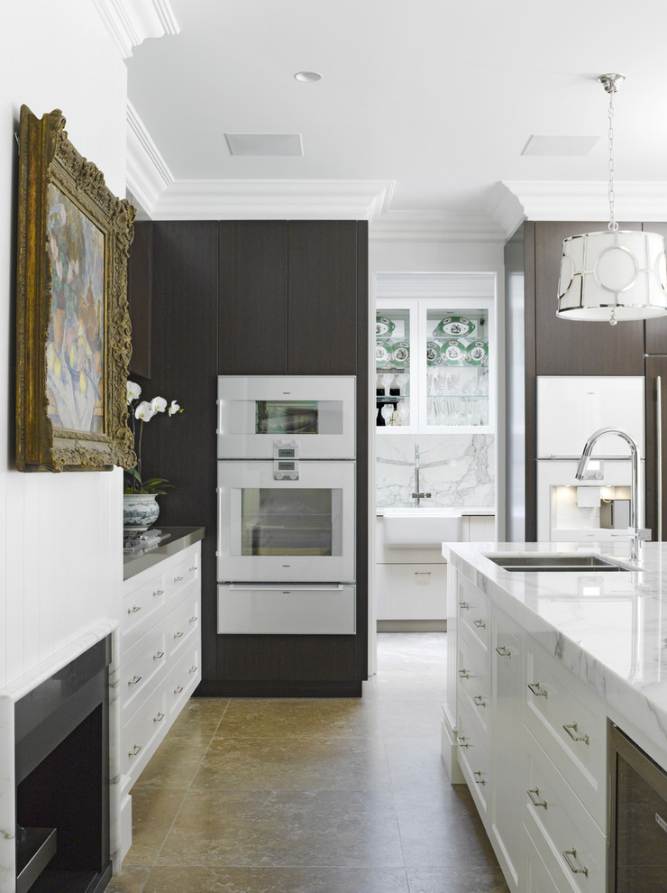 Exempel på ett stort klassiskt l-kök, med en undermonterad diskho, marmorbänkskiva, vita vitvaror, travertin golv och en köksö