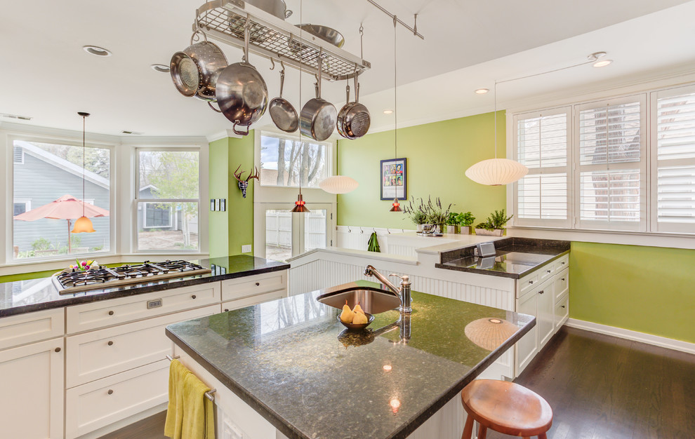 Foto på ett mellanstort funkis kök, med en dubbel diskho, luckor med upphöjd panel, vita skåp, granitbänkskiva, stänkskydd i stenkakel, rostfria vitvaror, mörkt trägolv och en köksö