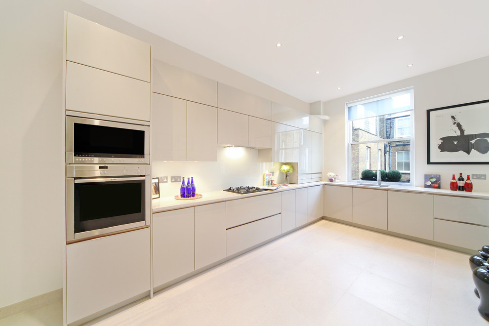 Inspiration for a large contemporary l-shaped kitchen/diner in London with an integrated sink, flat-panel cabinets, beige cabinets, granite worktops, beige splashback, glass sheet splashback, stainless steel appliances, limestone flooring and no island.