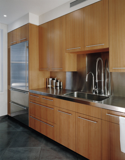 Modern inredning av ett kök, med en integrerad diskho, släta luckor, skåp i mellenmörkt trä, bänkskiva i rostfritt stål, rostfria vitvaror, stänkskydd med metallisk yta och stänkskydd i metallkakel