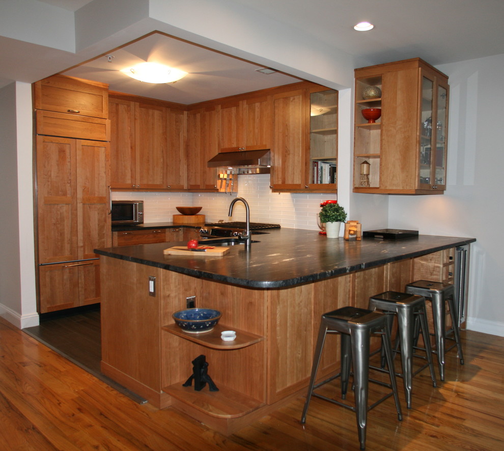 Inredning av ett klassiskt mellanstort svart svart kök, med en undermonterad diskho, skåp i shakerstil, skåp i mellenmörkt trä, granitbänkskiva, vitt stänkskydd, stänkskydd i glaskakel, rostfria vitvaror, klinkergolv i porslin, en halv köksö och brunt golv