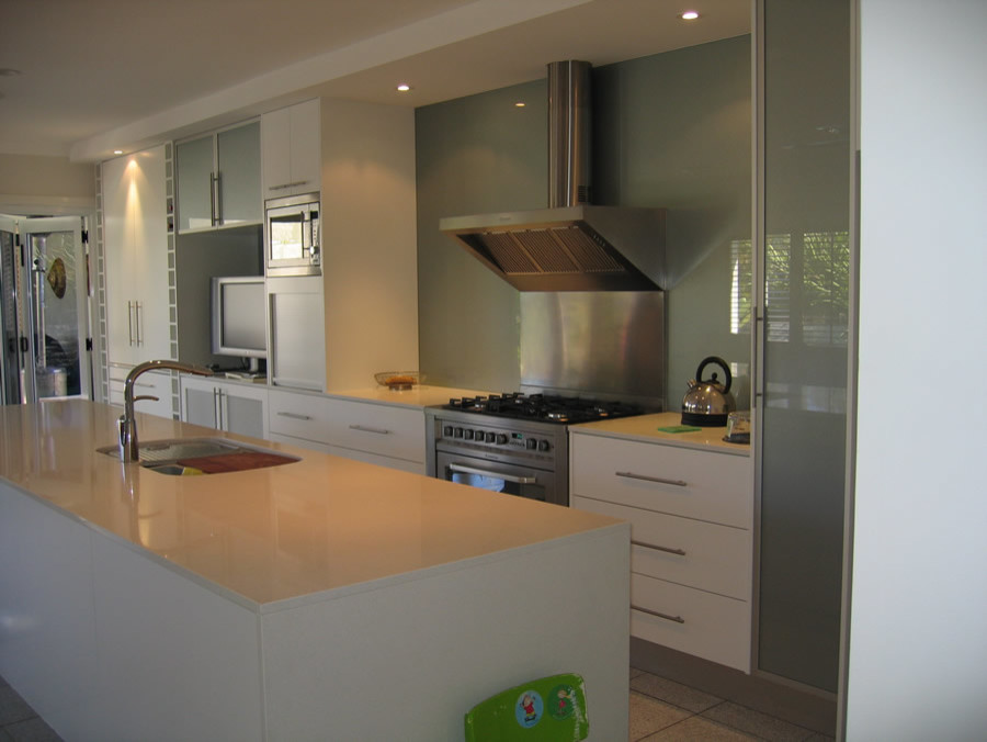 Bild på ett stort funkis linjärt kök och matrum, med en nedsänkt diskho, släta luckor, vita skåp, granitbänkskiva, grönt stänkskydd, glaspanel som stänkskydd, rostfria vitvaror, klinkergolv i keramik och en köksö